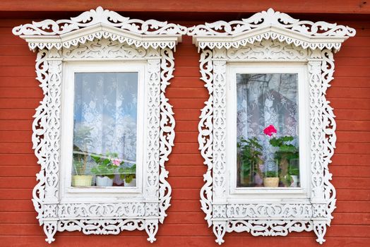 Two traditional Russian wooden window with flowers on windowsills