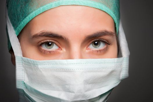 Closeup portrait of a female surgeon, with face mask, in a dark grey background