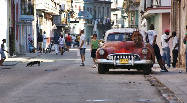 Central Havana, Street scene with old american car parked on the side with wooden boat on it, few people standing beside