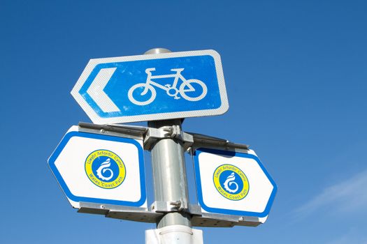 Signs for the 'Wales coast path' and for a cycle route against a bright blue sky.