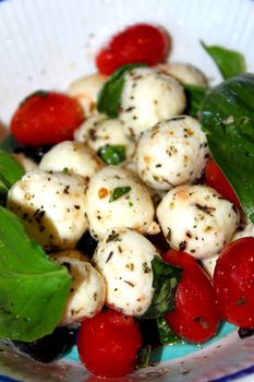 Closeup of a salad with mozarella balls with cherry tomatoes and basil.