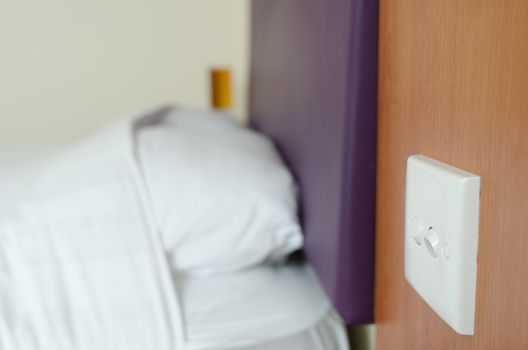 Lighting switch near bad with white pillows and cover