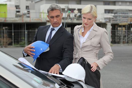 Male and female architects stood by car