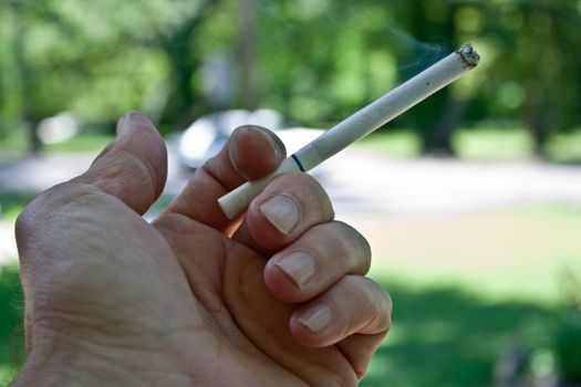 Close up of a hand holding a lite cigarette in the open.