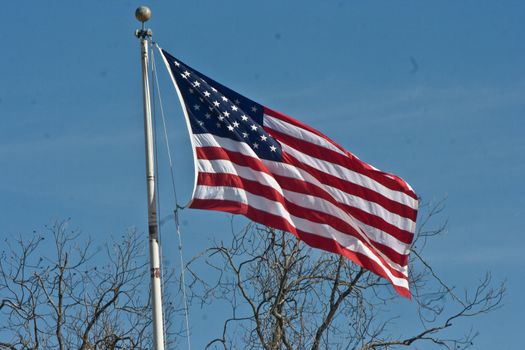 A single American flag stands high amongst a winter blue sky.