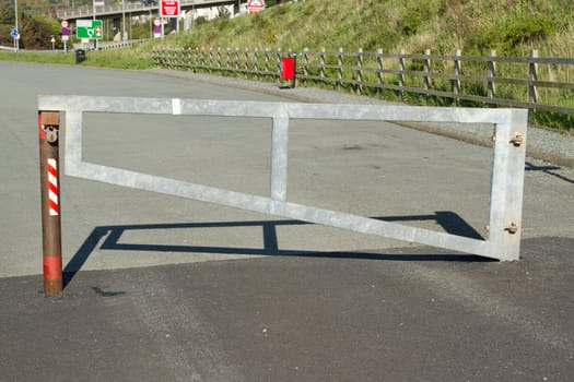 A metal gate, barrier closed and locked with a padlock on a tarmac road.