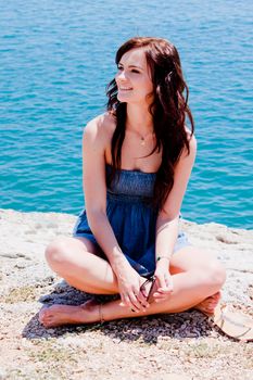 Young and beautiful girl resting on rocks against the sea