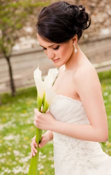 Beautiful bride with wedding dress holding white calla lilies looking down