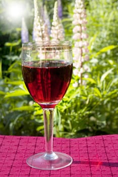 Red wine glass upon garden flowers background