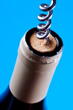Corkscrew in cork in wine bottle on blue background