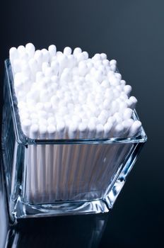 Cotton buds in a glass on a glass table on a dark background