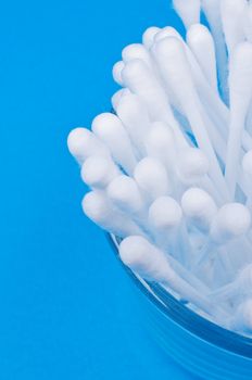 Cotton buds in glass on blue background close up