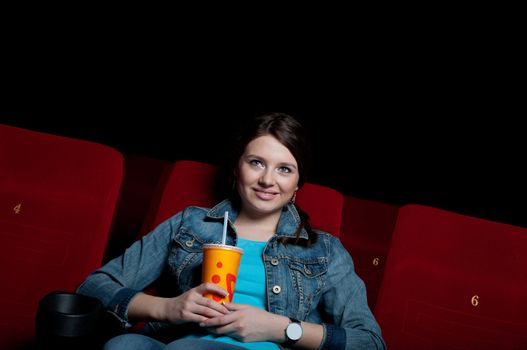 beautiful woman in a movie theater, watching a movie and drink a drink