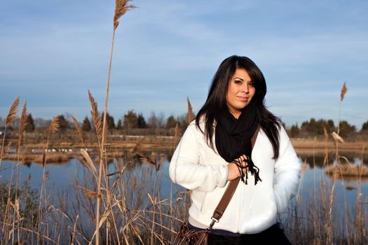 Portrait of a young Hispanic woman outdoors near a pond by the shoreline. 