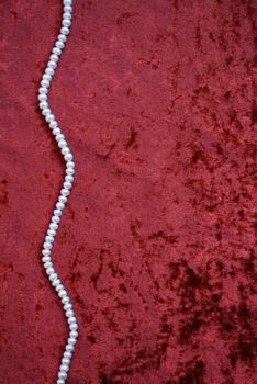 Necklace of white pearls on a terracotta velvet as background 