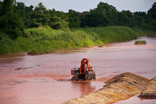 Excavator loader at river with raised bucket over blue sky