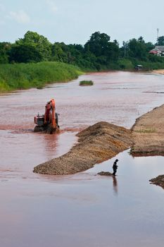 Excavator loader at river with raised bucket over blue sky