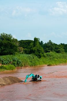 Excavator loader at river with raised bucket over blue sky