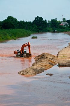 Excavator loader at river with raised bucket over blue sky