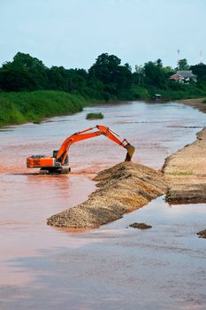 Excavator loader at river with raised bucket over blue sky