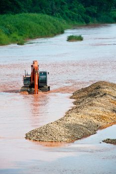 Excavator loader at river with raised bucket over blue sky