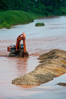 Excavator loader at river with raised bucket over blue sky