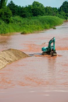 Excavator loader at river with raised bucket over blue sky