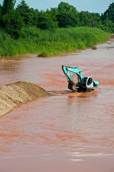 Excavator loader at river with raised bucket over blue sky