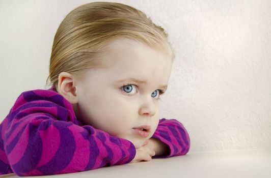 Adorable young girl with resting her head on her folded hands against a white background.