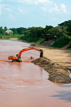 Excavator loader at river with raised bucket over blue sky