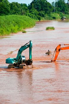 Excavator loader at river with raised bucket over blue sky