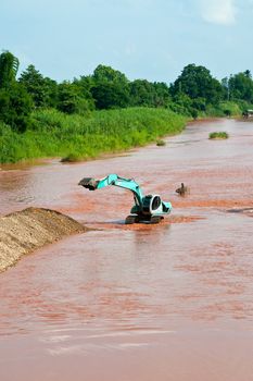 Excavator loader at river with raised bucket over blue sky