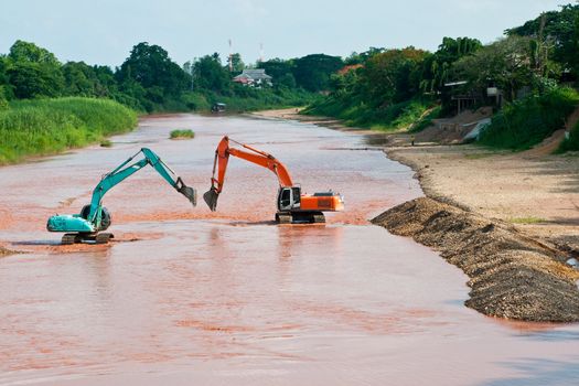 Excavator loader at river with raised bucket over blue sky