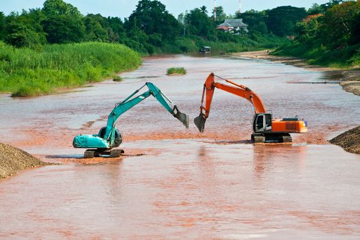 Excavator loader at river with raised bucket over blue sky