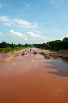 Excavator loader at river with raised bucket over blue sky