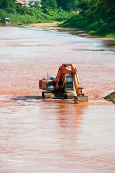 Excavator loader at river with raised bucket over blue sky