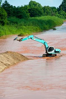 Excavator loader at river with raised bucket over blue sky