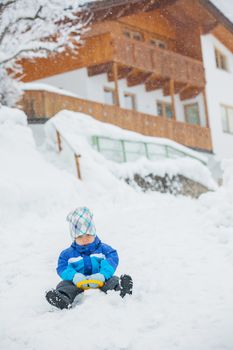 Cute little boy in blue riding on a sled near  the Austrian cottage