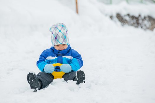 Cute little boy in blue riding on a sled near  the Austrian cottage