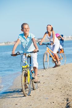 Cute girl with her mother and brother ride bikes along the beach. Focus on girl. Vertical view