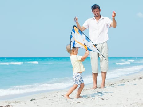 Little cute boy playing his father with a colorful kite on the tropical beach.