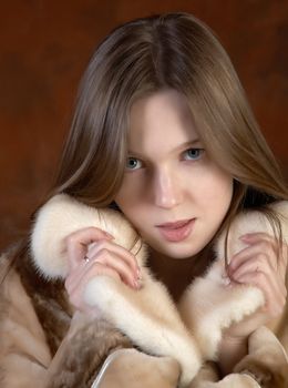 The girl in a fur coat on motley background in studio