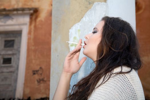 Beautiful plus size woman smokes  cigarette against an old building