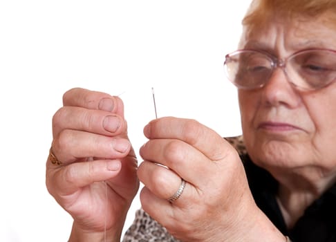 The old woman passes  thread in needle on  white background
