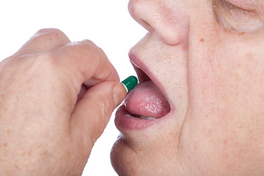 old woman puts  capsule with medicines in  mouth on a white background