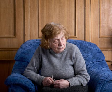 The old woman sits in an armchair at home