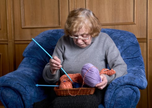 The old woman sits in an armchair and knits