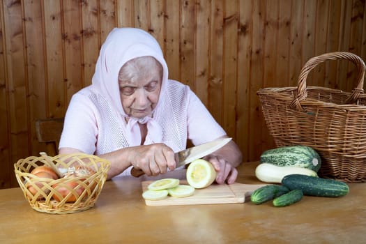 The old woman cuts  vegetable marrow on a table