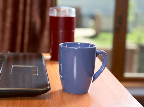  laptop coffee grinder and  cup on a desk in the solar morning