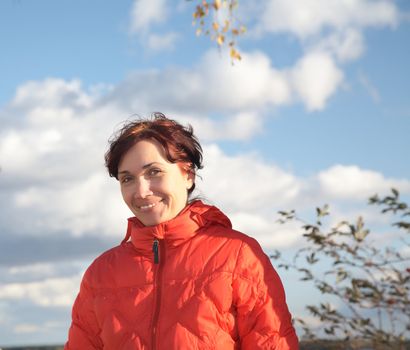 A smiling woman in  red jacket on  background of the blue sky